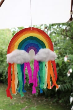 a rainbow and cloud mobile hanging from a tree in front of some trees with clouds