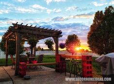 an outdoor dining area with red chairs and wooden pergoline structure at sunset in the background