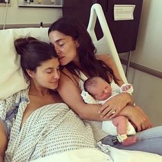 two women and a baby are laying in a hospital bed with their arms around each other