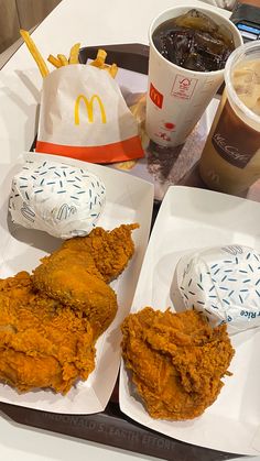 two trays filled with fried chicken next to cups of soda and drinks on a table