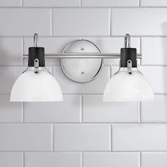 two lights are mounted on the wall next to a white tiled wall in a bathroom