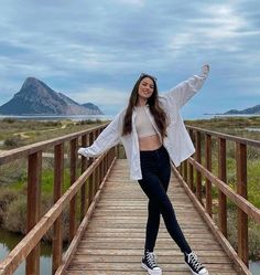 a woman standing on a wooden bridge with her arms out and hands in the air