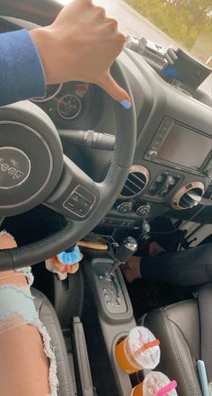 a person driving a car with their hand on the steering wheel and cup holders in front of them