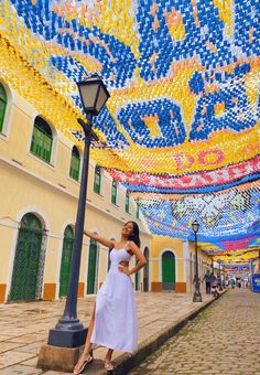 a woman in white dress standing next to a lamp post and colorful decorations on the ceiling