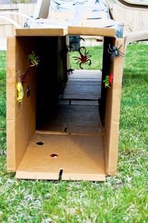 an open cardboard box with spider decorations on the inside sitting in grass next to a chair