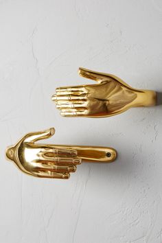 two gold hand shaped objects on a white wall