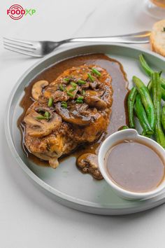 a white plate topped with meat covered in mushroom gravy next to green beans