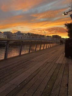 the sun is setting at the end of the pier with people walking on it and buildings in the background