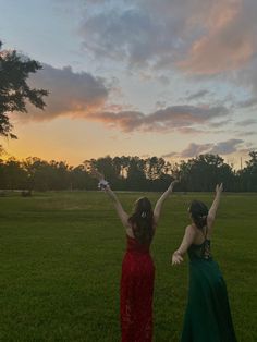 two women in dresses are standing on the grass with their arms up and hands raised