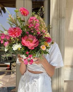 a woman holding a bouquet of flowers in front of her face while wearing a white dress