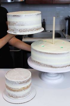 a woman standing in front of a cake on top of a white counter next to two cakes