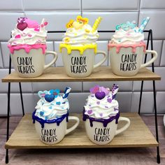 three mugs with candy hearts on them are sitting on a wooden shelf in front of a tile wall