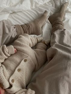 a baby laying on top of a bed wearing a sweater and pants with two feet in the air