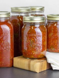 four jars filled with red sauce sitting on top of a wooden cutting board