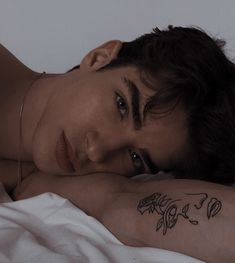 a woman laying on top of a bed next to a white wall with tattoos on her arm