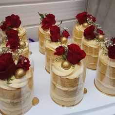 there are many small cakes with red flowers on top of each cake, and gold balls in the middle