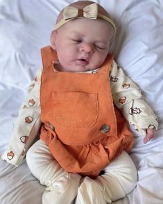 a baby wearing an orange bib laying on top of a bed