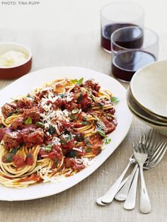 a white plate topped with pasta and sauce next to silverware on top of a table