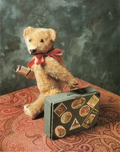 a teddy bear sitting on top of an old suitcase with stickers all over it