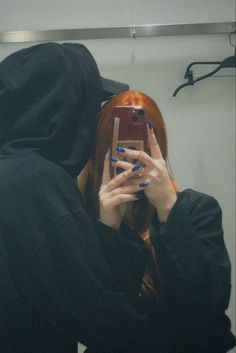 a woman with red hair taking a selfie in front of a mirror while wearing a black hoodie