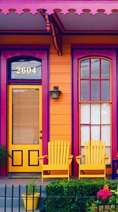 two yellow chairs sitting in front of a purple and orange building with red trim on the windows