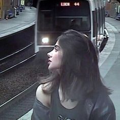 a woman standing in front of a train at a station with her head turned to the side