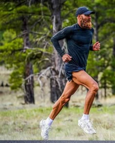 a man with a beard running in the grass and trees behind him is wearing white sneakers