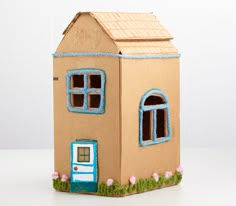 a cardboard doll house with blue windows and pink flowers on the outside, in front of a white background