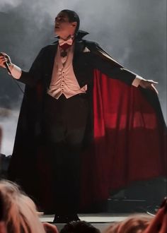 a man dressed as dracula standing on stage with his hands out to the side,