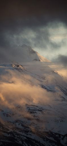 an airplane is flying in the sky over some snow covered mountains and clouds at sunset