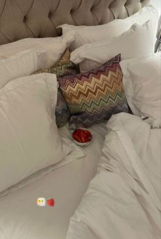 a bed with white sheets, pillows and a bowl of strawberries on the pillow