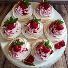 a white plate topped with cupcakes covered in frosting and raspberries