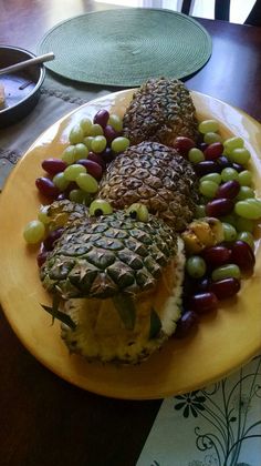 pineapples, grapes and other fruit are arranged on a yellow plate at the table