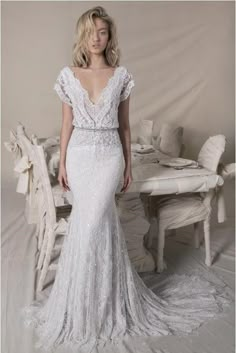 a woman standing in front of a table wearing a wedding dress with an open back