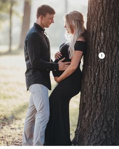 a man and woman standing next to each other near a tree in the woods with their arms around each other