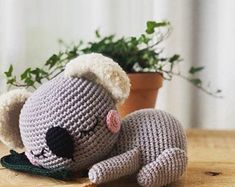 a crocheted stuffed animal laying on top of a wooden table next to a potted plant