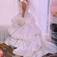 a woman in a white wedding dress standing next to a window with her veil pulled back