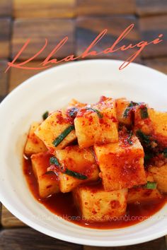 a white bowl filled with tofu and sauce on top of a wooden table next to chopsticks