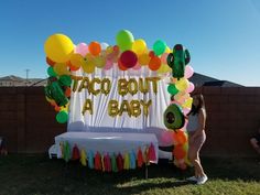 a woman standing in front of a taco bouta baby sign with balloons on it