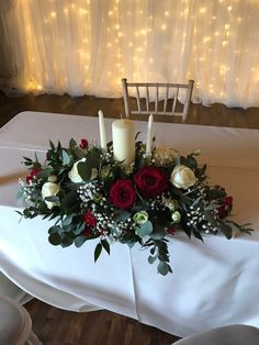 a centerpiece with roses and greenery on a white table cloth at a wedding reception