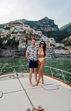 a man and woman standing on the bow of a boat in front of a city