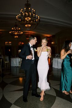 a man and woman standing next to each other at a formal event with chandeliers in the background