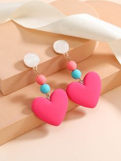 two heart shaped earrings on top of a pink box next to a white bow tie