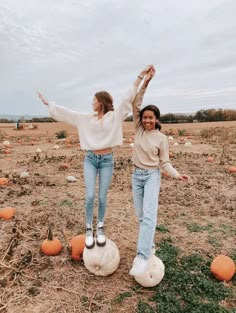 two women standing on top of pumpkins in an open field with their arms outstretched