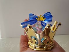 a hand holding a gold crown with candy in it's middle and a blue bow on the top