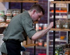 a man standing in front of a shelf filled with jars and other food items on shelves