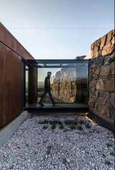 a man walking in front of a building with rocks and grass on the ground next to it