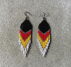 two pairs of beaded earrings with black, yellow and red beads on grey carpet