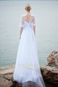 a woman in a white dress standing on rocks near the water looking at the ocean