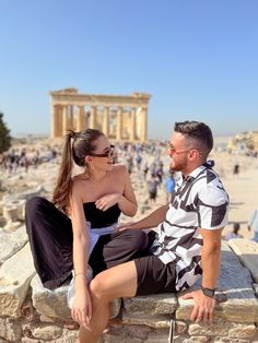 a man and woman sitting on a stone wall in front of the parthenion